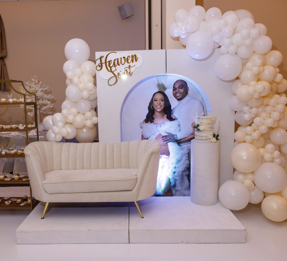 White arched backdrop with gold Heaven Sent script, a couple's portrait, an ivory loveseat and an organic ivory balloon garland