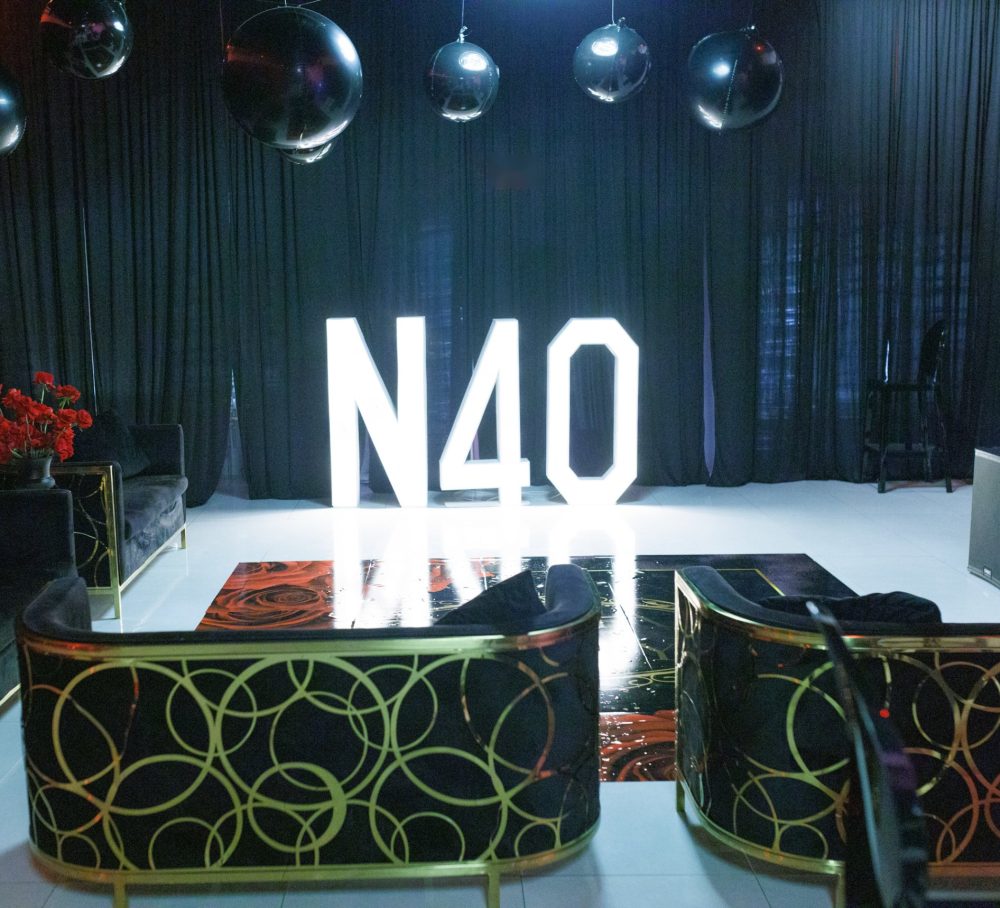Giant lit marquee letters spelling N40 in front of black drapes, with black-and-gold lounge seating